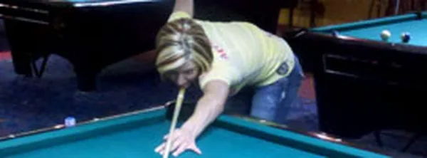 A woman taking a shot during a game at Cue's Billiards